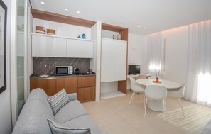 Eine moderne Küche mit Mikrowelle, Wasserkocher und Schränken. Es gibt einen Essbereich mit Tisch und Stühlen sowie eine Wohnbereich mit einer Couch.