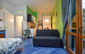 Ein kleines Zimmer mit Bett, Stuhl, Küchenzeile und Essecke.