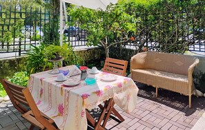 An outdoor patio with a table set for dining, surrounded by greenery and a wicker chair. - Stunning apartment in Viareggio with WiFi (Viareggio)