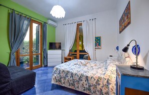 Ein Schlafzimmer mit Bett, Schreibtisch, Stuhl, Fernseher und einem Fenster mit Vorhängen.