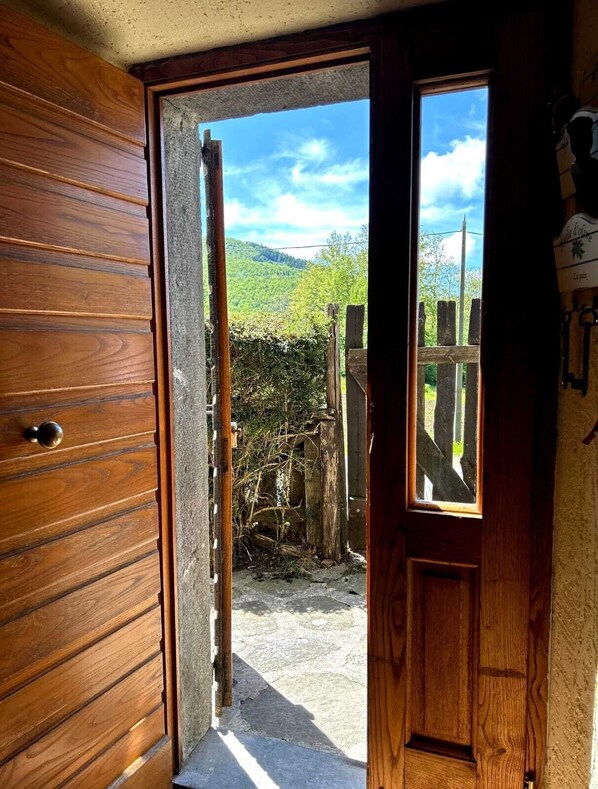 A wooden door leading to a garden with a view of a hill and a clear sky.
