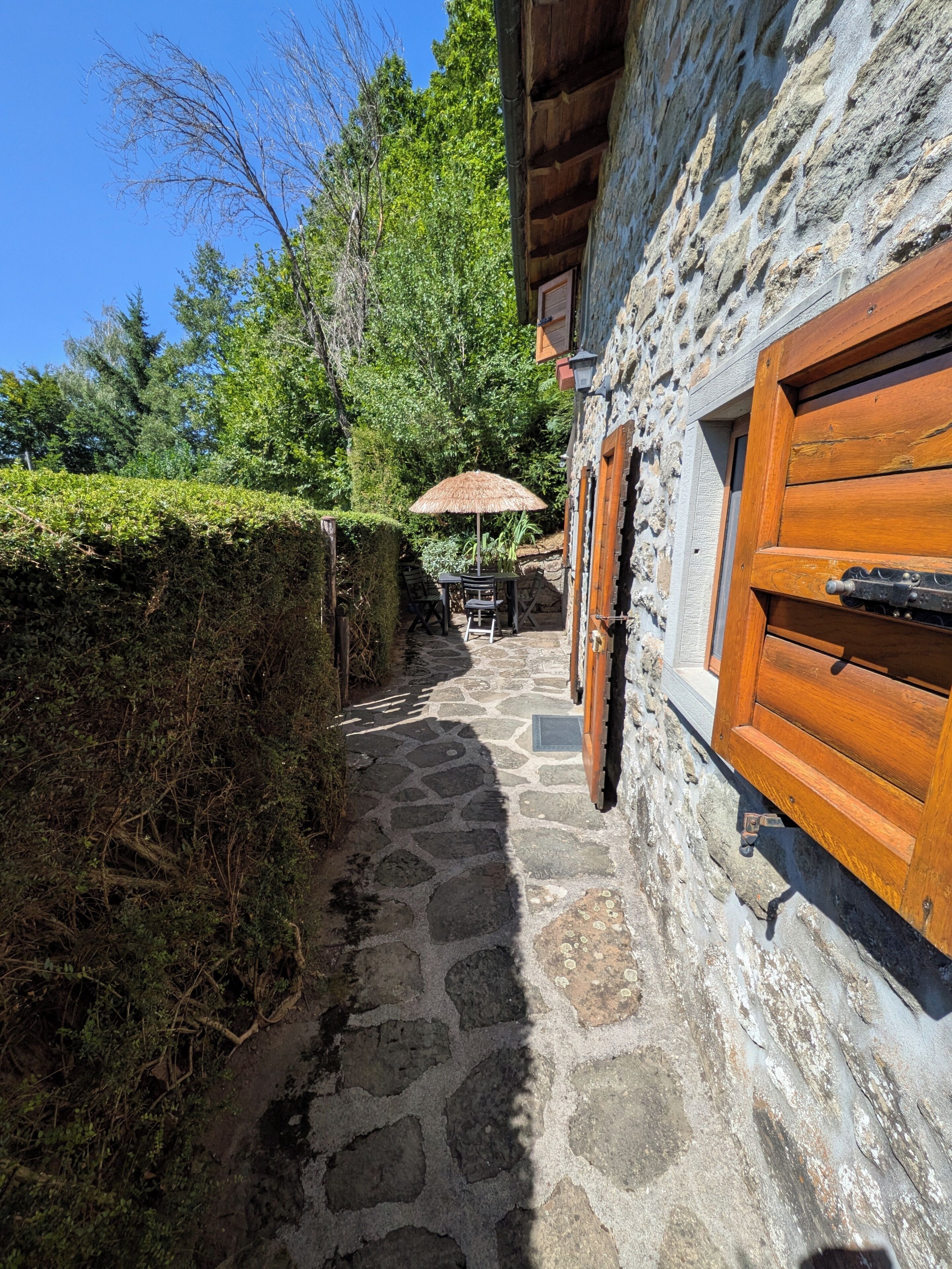 A stone pathway leading to a wooden door with a thatched umbrella, surrounded by greenery and trees.
