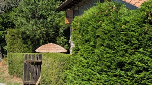 Une maison avec une façade en pierre, un portail en bois et un parasol en chaume.