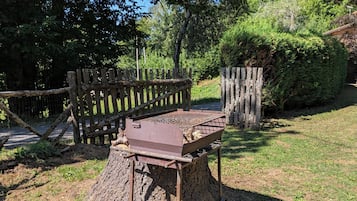 Un'area barbecue rustica all'aperto su un ceppo, circondata da un recinto in legno e vegetazione rigogliosa.
