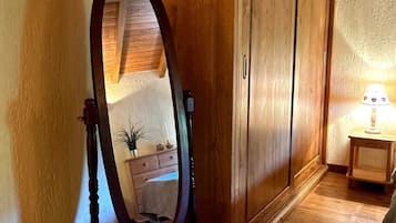 Ein Zimmer mit Holzboden, einem Holzschrank, einem anstehenden Spiegel und einem kleinen Tisch mit einer Lampe.