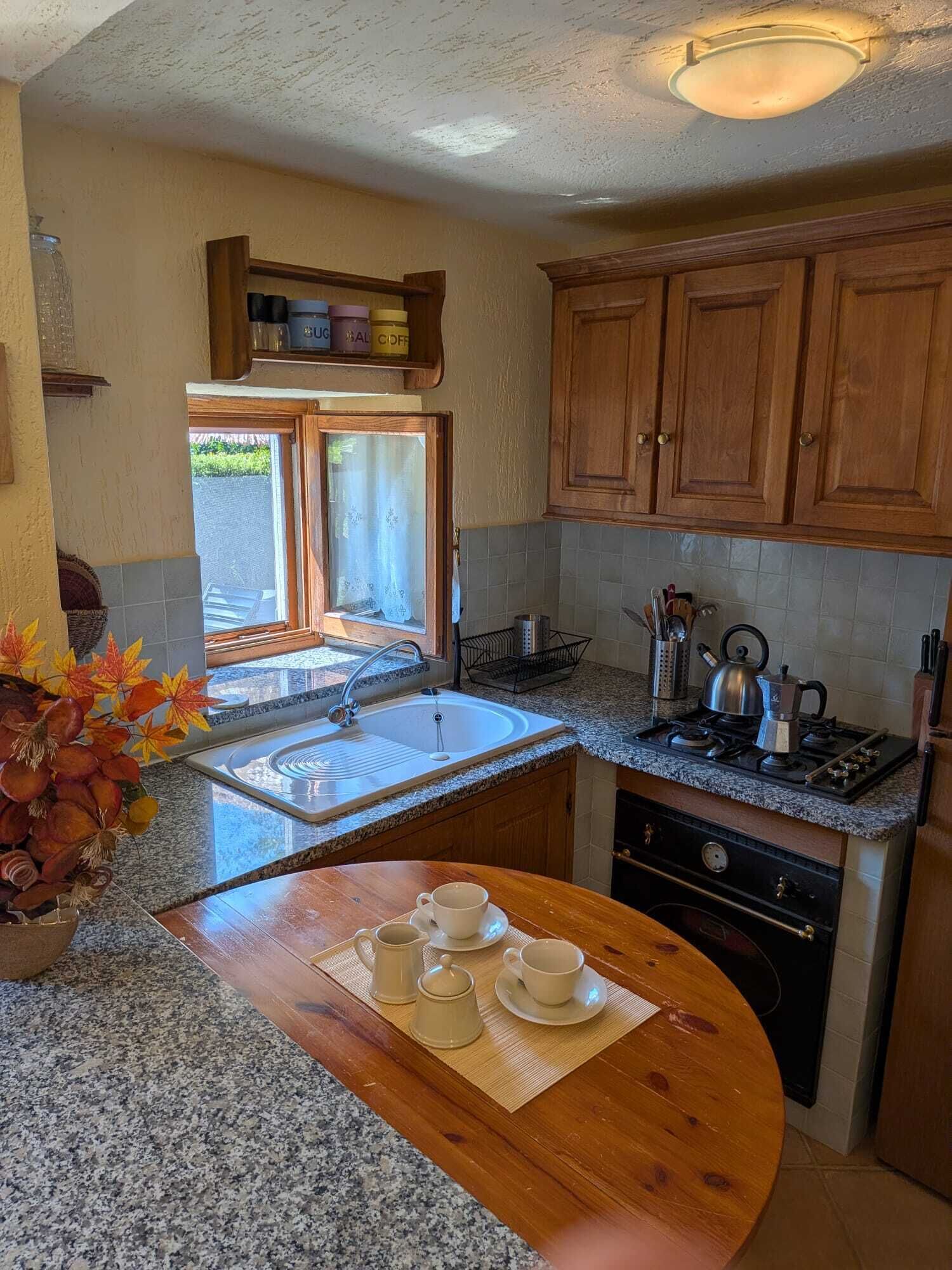 Una cucina con mobili in legno, un piano di lavoro in granito, un lavello, un fornello e una finestra con vista.