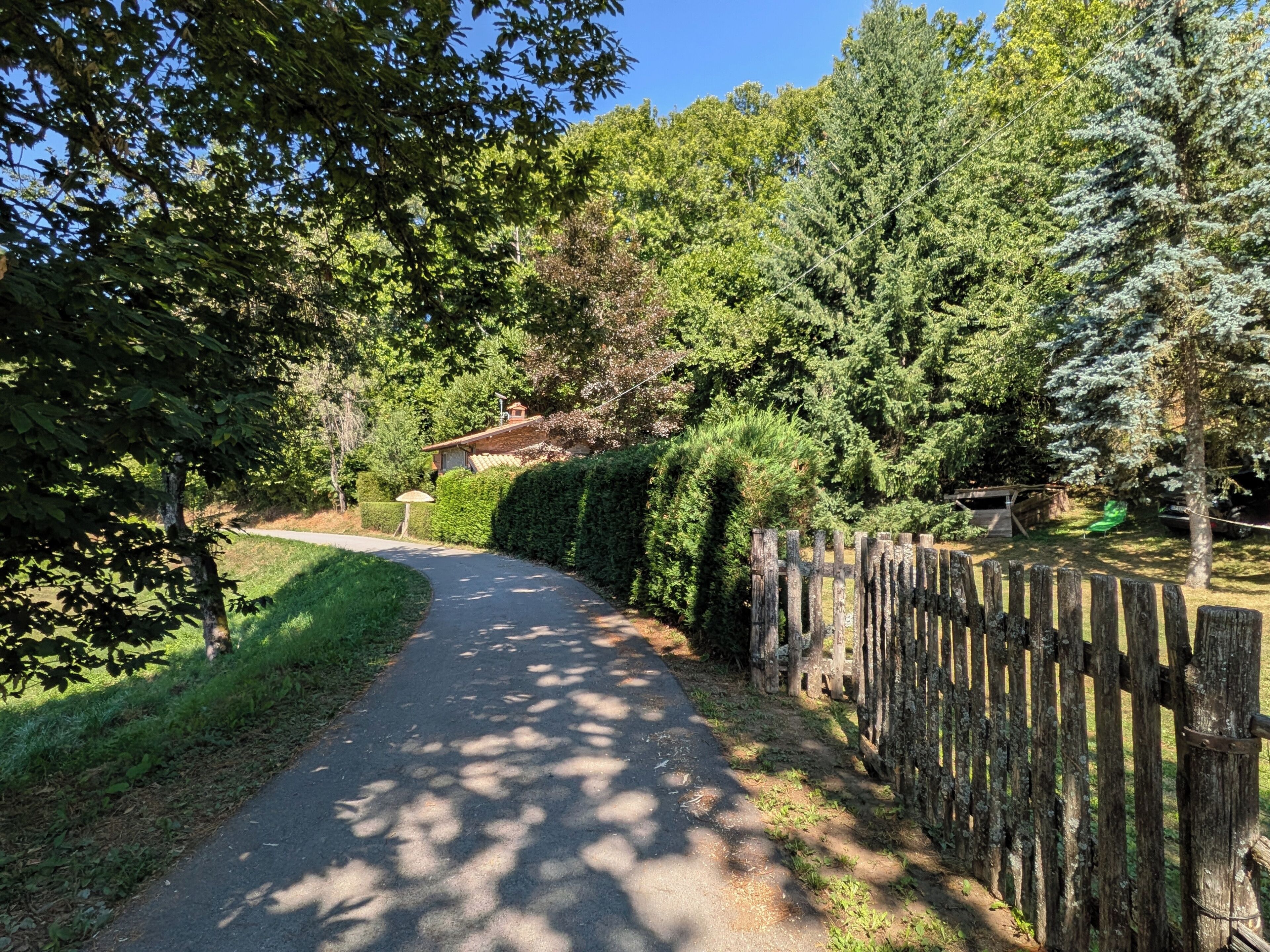 Un chemin pavé, bordé de clôtures en bois et d’une végétation luxuriante, mène à un bâtiment dont le toit est rouge.