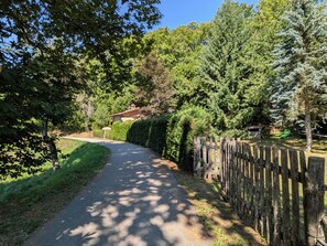 Un chemin pavé, bordé de clôtures en bois et d’une végétation luxuriante, mène à un bâtiment dont le toit est rouge.