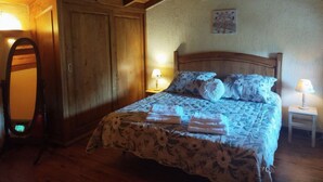Une chambre avec un plafond en bois, un lit recouvert d’une literie à motifs floraux, une armoire et un miroir.