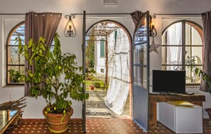 Ein Zimmer mit Fernseher, einer Topfpflanze und Blick auf einen Garten durch einen Rundbogen.