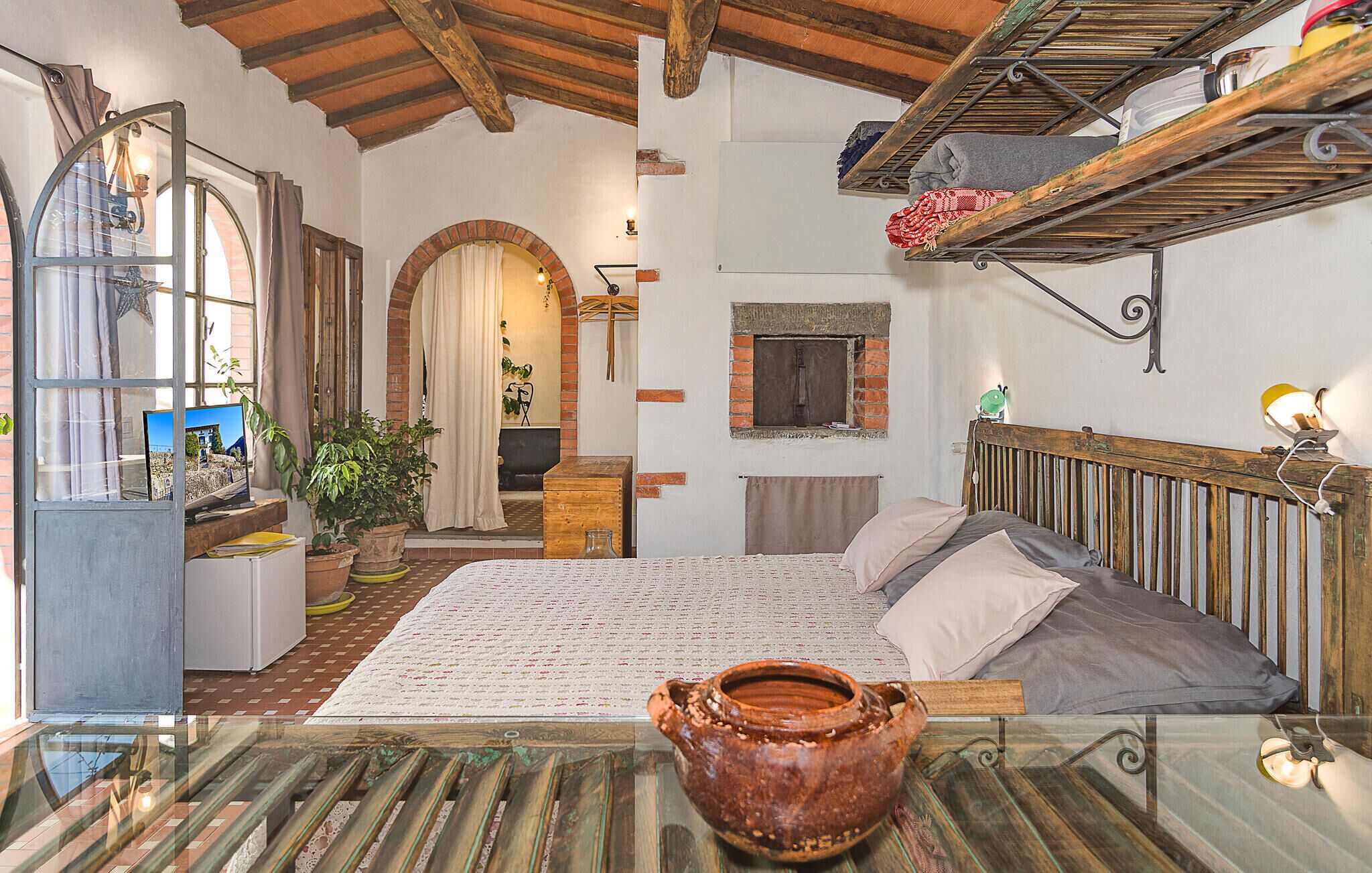 Ein gemütliches Schlafzimmer mit Bett, Holz-Kopfteil, rustikaler Ziegelwand, kleinem Fenster und einer Ablage mit Gegenständen.