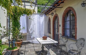 En udendørs patio med et bord og stole, plantekasser og et overdækket område med et hvidt gardin.
