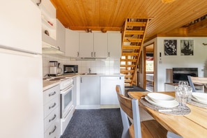 A compact kitchen with white cabinets, a microwave, a stove, and a sink. There's a wooden staircase leading to a dining area with a table set for two.