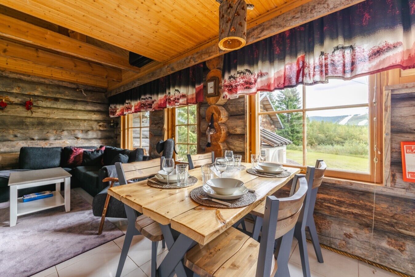 A rustic wooden interior with a dining table set for four, a sofa, and a fireplace.