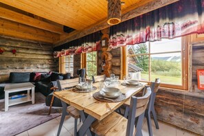 A rustic wooden interior with a dining table set for four, a sofa, and a fireplace.