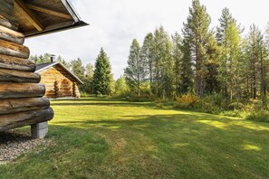 A log cabin with a grassy yard and a forested backdrop.