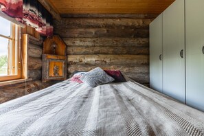 A log cabin bedroom with a bed, a nightstand, a window, and a wardrobe.
