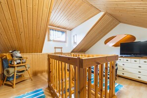 A loft bedroom with a wooden ceiling, a television, a wooden crib, and a window.