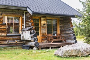 A log cabin with a porch, a bench, and a large rock in front.