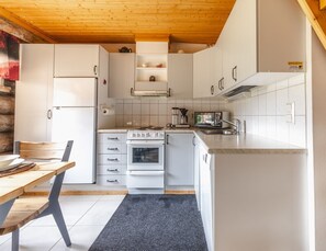 A modern kitchen with white cabinetry, a wooden ceiling, and a dining area with a table and chairs.