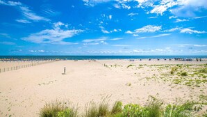 En bred, sandet strand med en klar blå himmel og spredte skyer.