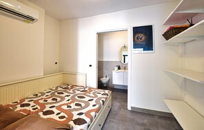 A bedroom with a bed, a bedside table, a wardrobe, a bathroom with a sink and mirror, and a shelf with items. - Cozy apartment in Chioggia with WiFi (Chioggia)