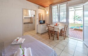 Ein Zimmer mit einem Bett, einem Esstisch mit Stühlen, einer Küchenzeile und einer Glastür, die auf eine Terrasse im Freien führt.