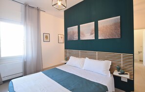 A bedroom with a bed, a nightstand, a window with curtains, and wall-mounted artwork. - Le Vele - Contro Fiocco (Rosolina)