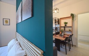 Ein modernes Schlafzimmer mit einem Bett, einer Akzentwand in Türkisgrün und einem Essbereich mit Tisch und Stühlen.