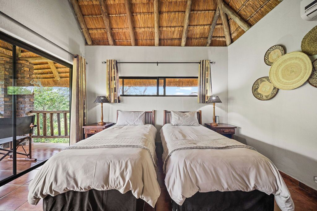 Une chambre avec deux lits, une fenêtre et un balcon équipé d’une table et de chaises.