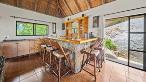 A kitchen with a stone island, wooden chairs, a thatched roof, and a view of a rocky landscape. - Boulders Bush Lodge: A Private Boulder-Top Retreat in Greater Kruger (Mica)