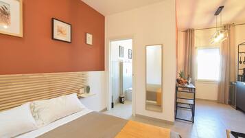 Une chambre d’hôtel comprenant un lit, une table de chevet, un miroir, une fenêtre avec des rideaux et un coin cuisine.