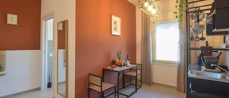 A modern kitchen with a dining area, a window with curtains, and a hanging plant.