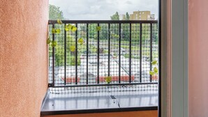 A balcony with a metal railing, a view of a parking lot, and a grassy area. - RentPlanet - Apartament Obozowa (Warszawa)