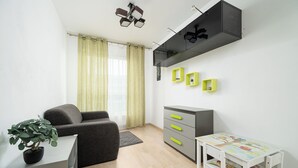 A compact living space with a sofa, a small table, a cabinet, and a potted plant. - RentPlanet - Apartament Obozowa (Warszawa)