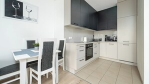 A compact kitchen with white cabinets, a dining table with chairs, and a small countertop with a kettle and a microwave. - RentPlanet - Apartament Obozowa (Warszawa)