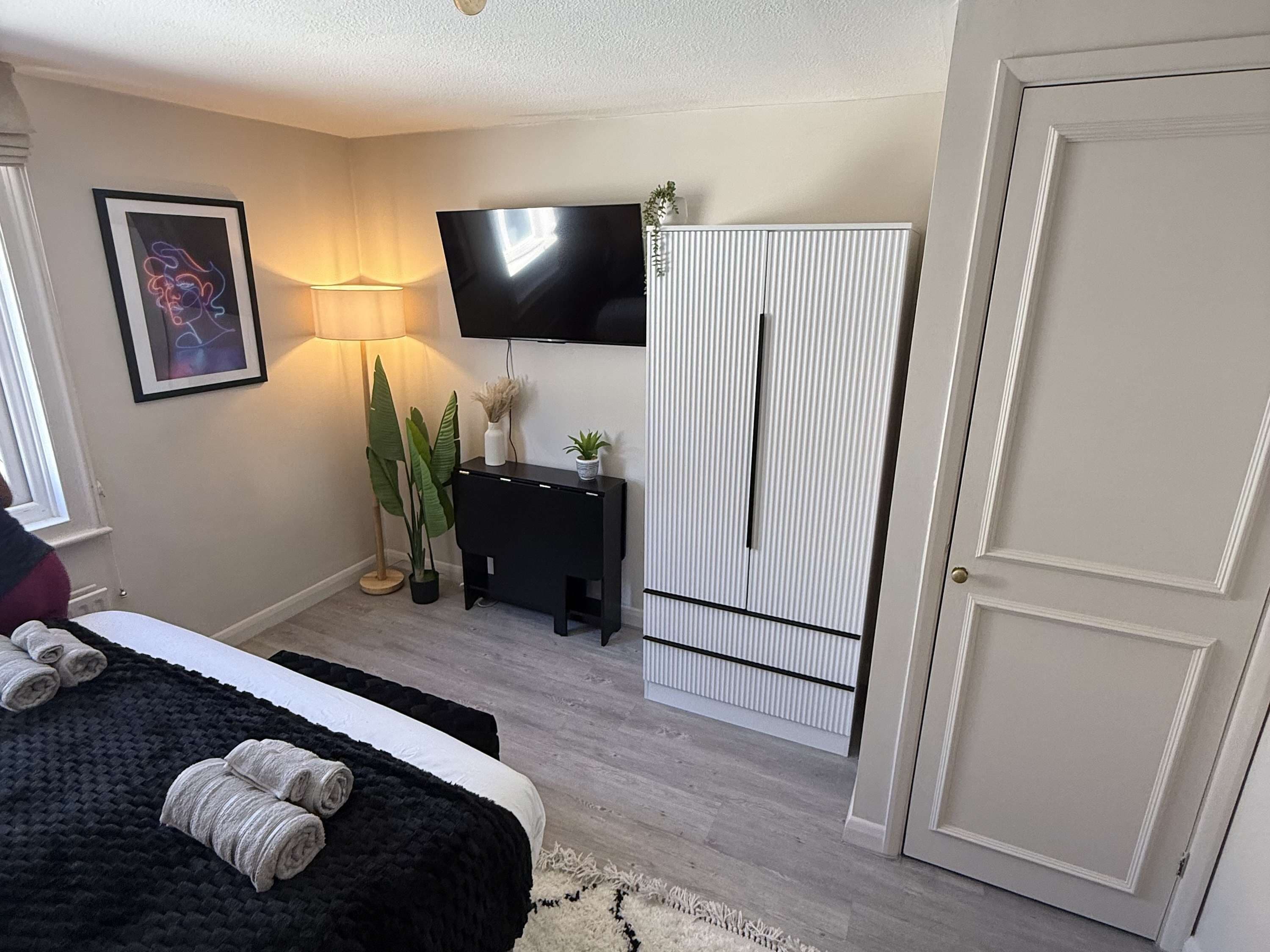 A bedroom with a bed, a TV, a wardrobe, a lamp, and a plant.