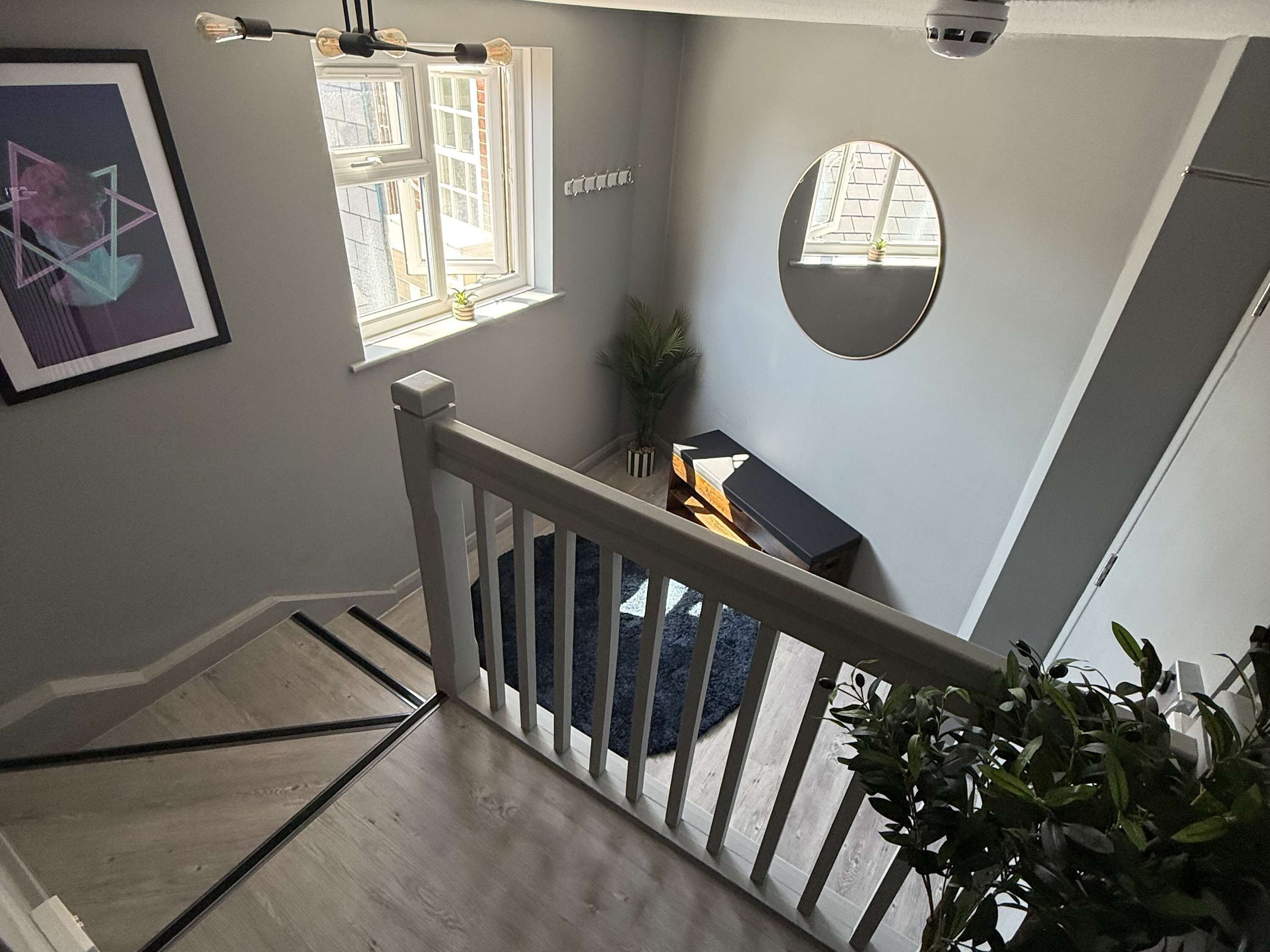 Un escalier avec une rampe en bois, un tableau encadré au mur et un miroir rond.