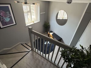 A staircase with a wooden handrail, a framed picture on the wall, and a round mirror.