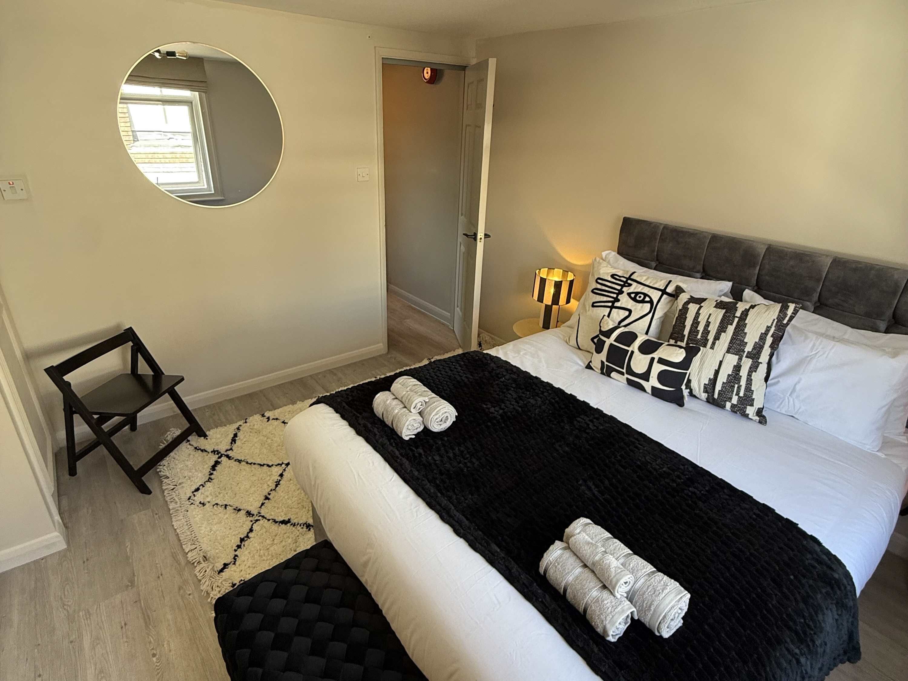 Une chambre à coucher avec un lit, un miroir rond, une lampe de chevet et une petite chaise.