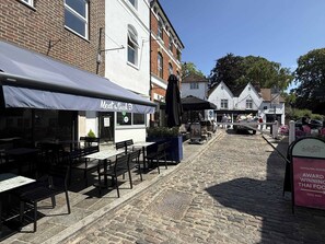 Una calle adoquinada con mesas al aire libre en un restaurante llamado 'Meat the Greek'.