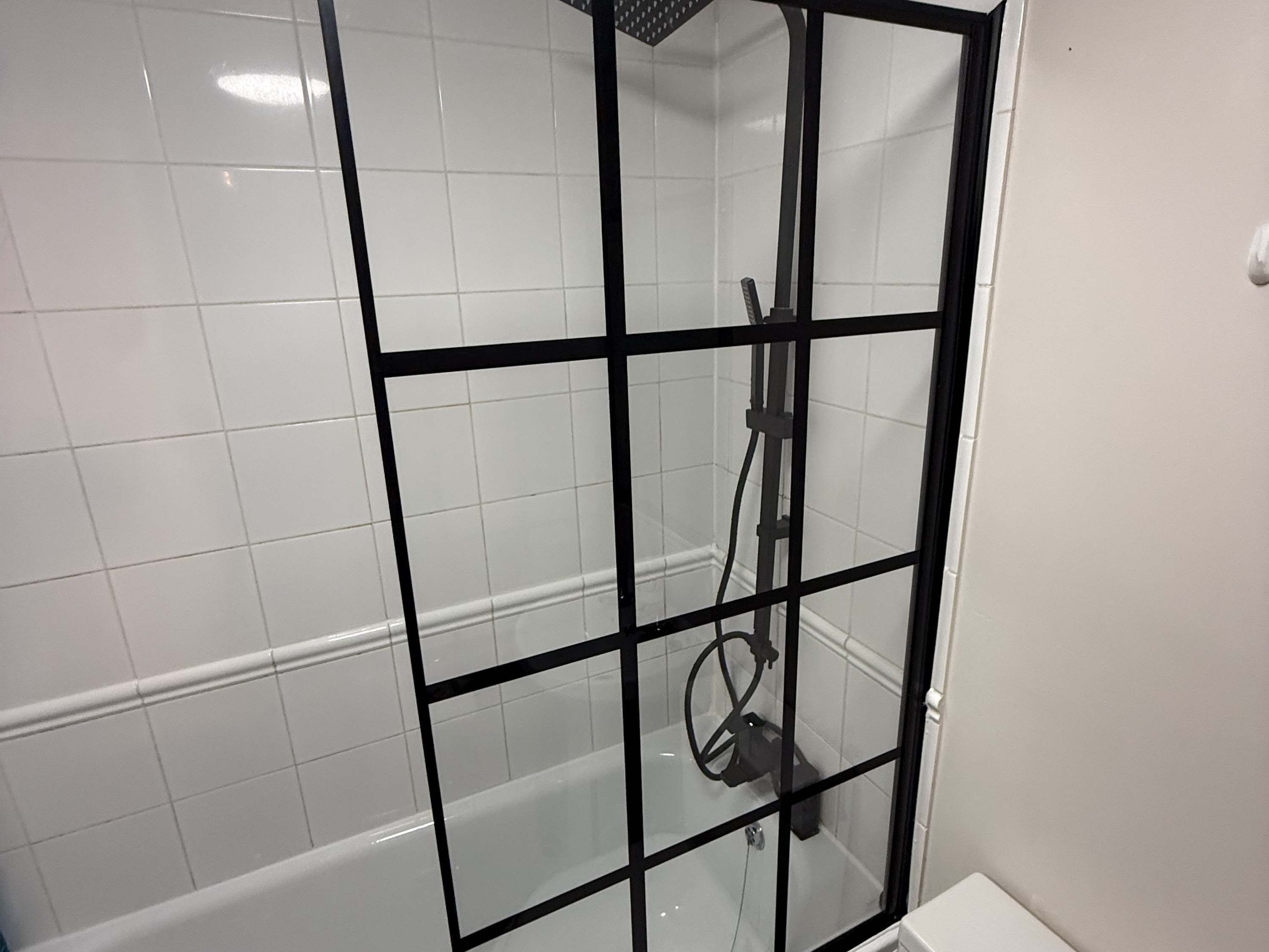 A bathroom with a glass-enclosed shower area, white tiled walls, and a white bathtub.