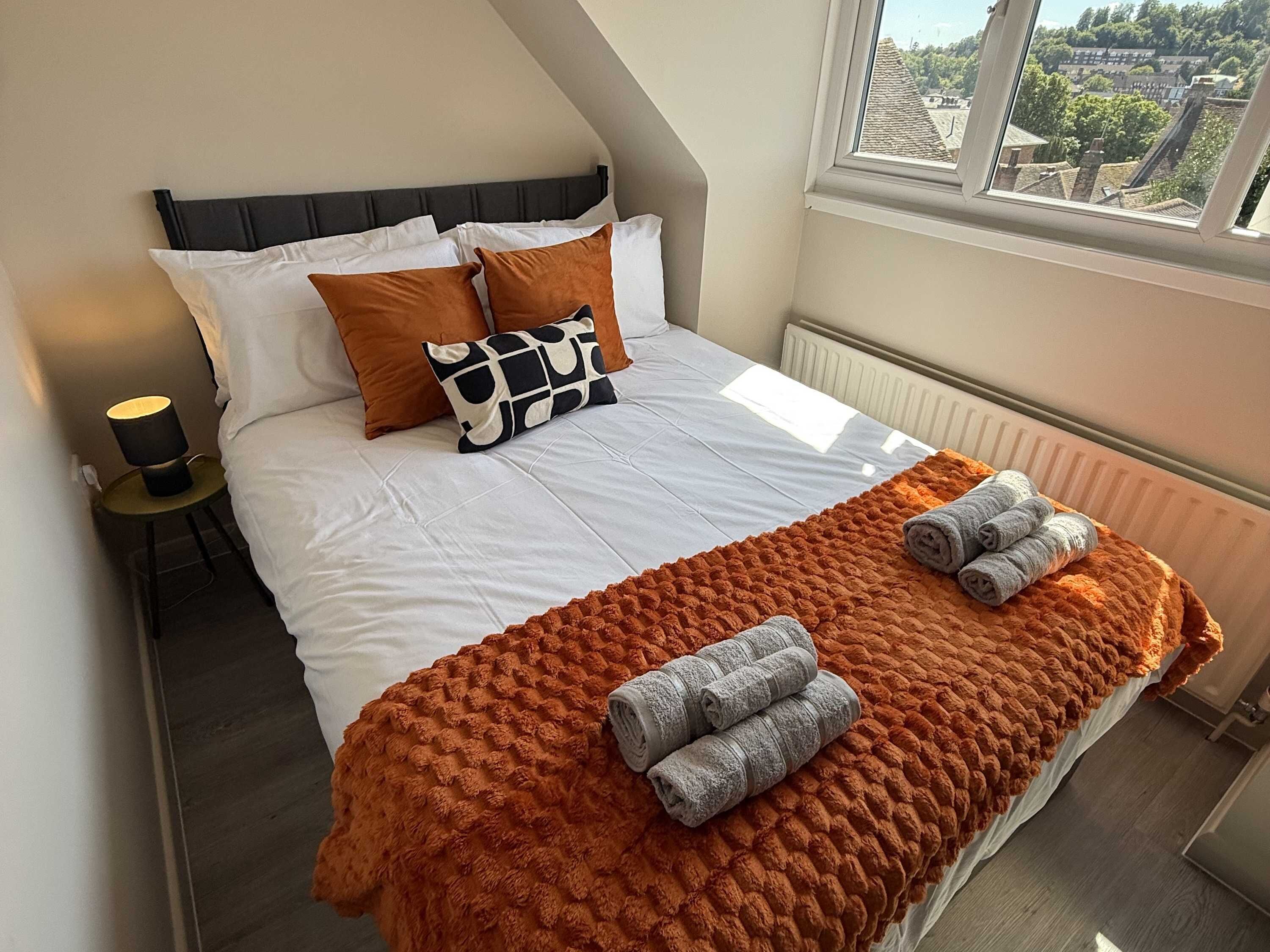 Un lit bien fait, avec une couette blanche, des oreillers marron et une couverture marron à texture. Des serviettes enroulées sont posées sur la couverture.