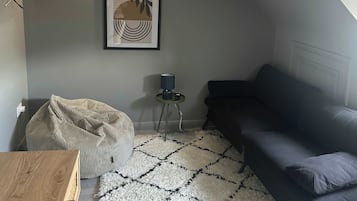 Une pièce avec un canapé de couleur sombre, une petite table d’appoint avec une lampe, un fauteuil en forme de poire, une œuvre d’art encadrée au mur et une table en bois.