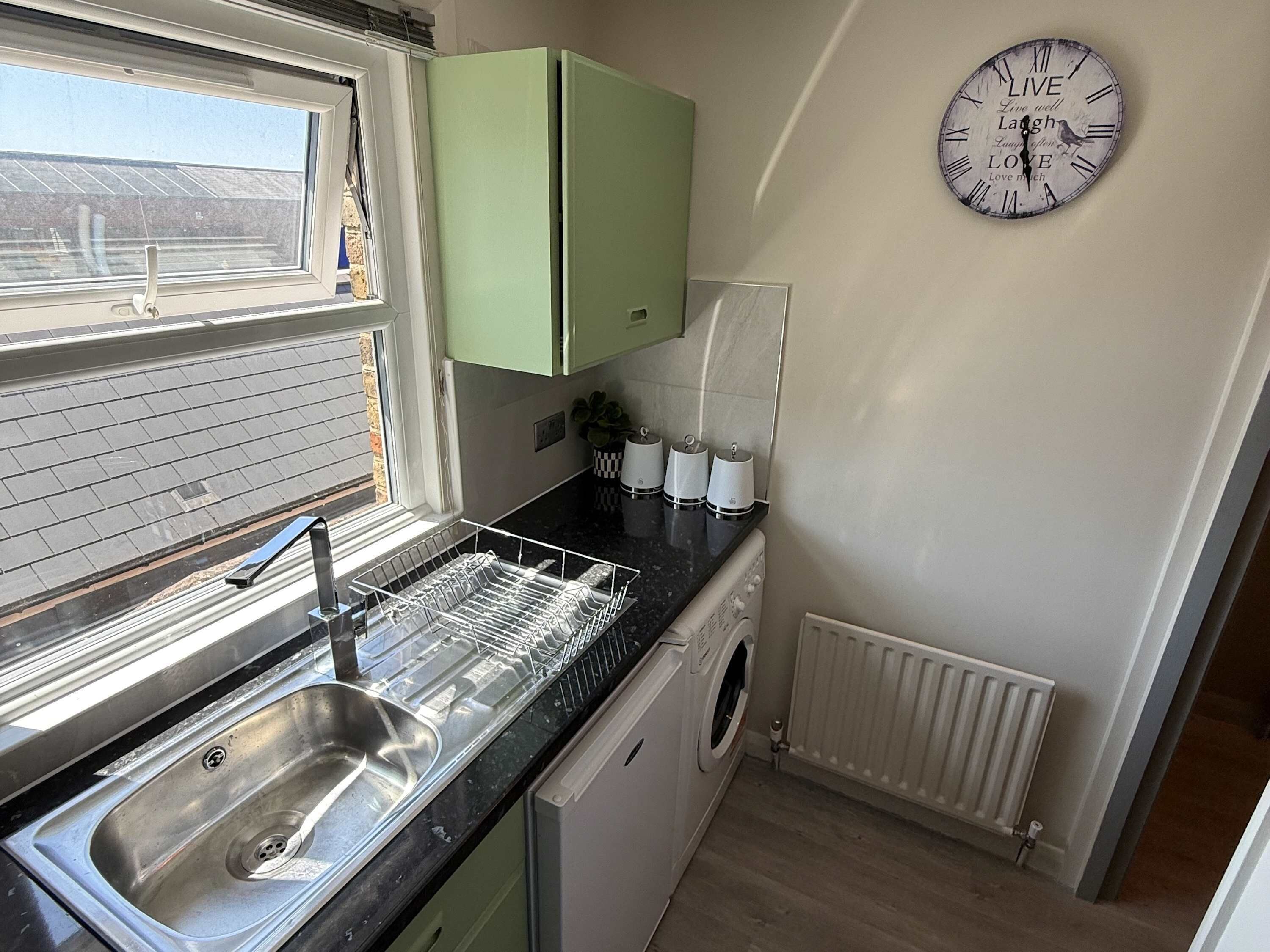 A compact kitchen with a sink, dishwasher, and a clock on the wall.