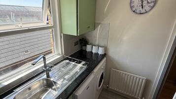 A compact kitchen with a sink, dishwasher, and a clock on the wall.