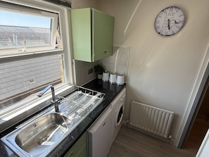 A compact kitchen with a sink, dishwasher, and a clock on the wall.