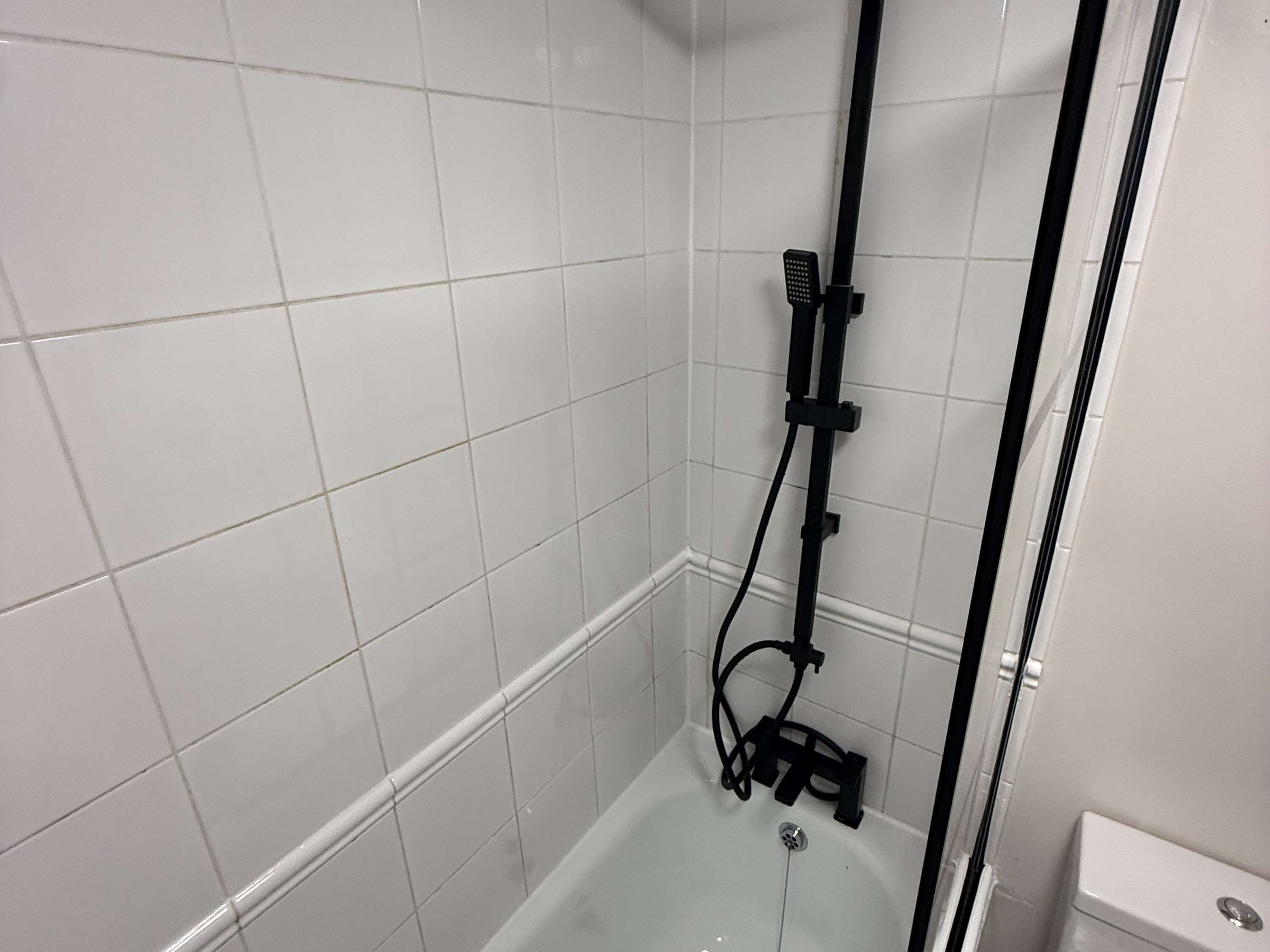 A bathroom with white tiled walls, a bathtub, and a shower area with a handheld showerhead.