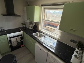 Cocina con encimera negra, lavavajillas y ventana con vistas a un edificio de ladrillo.