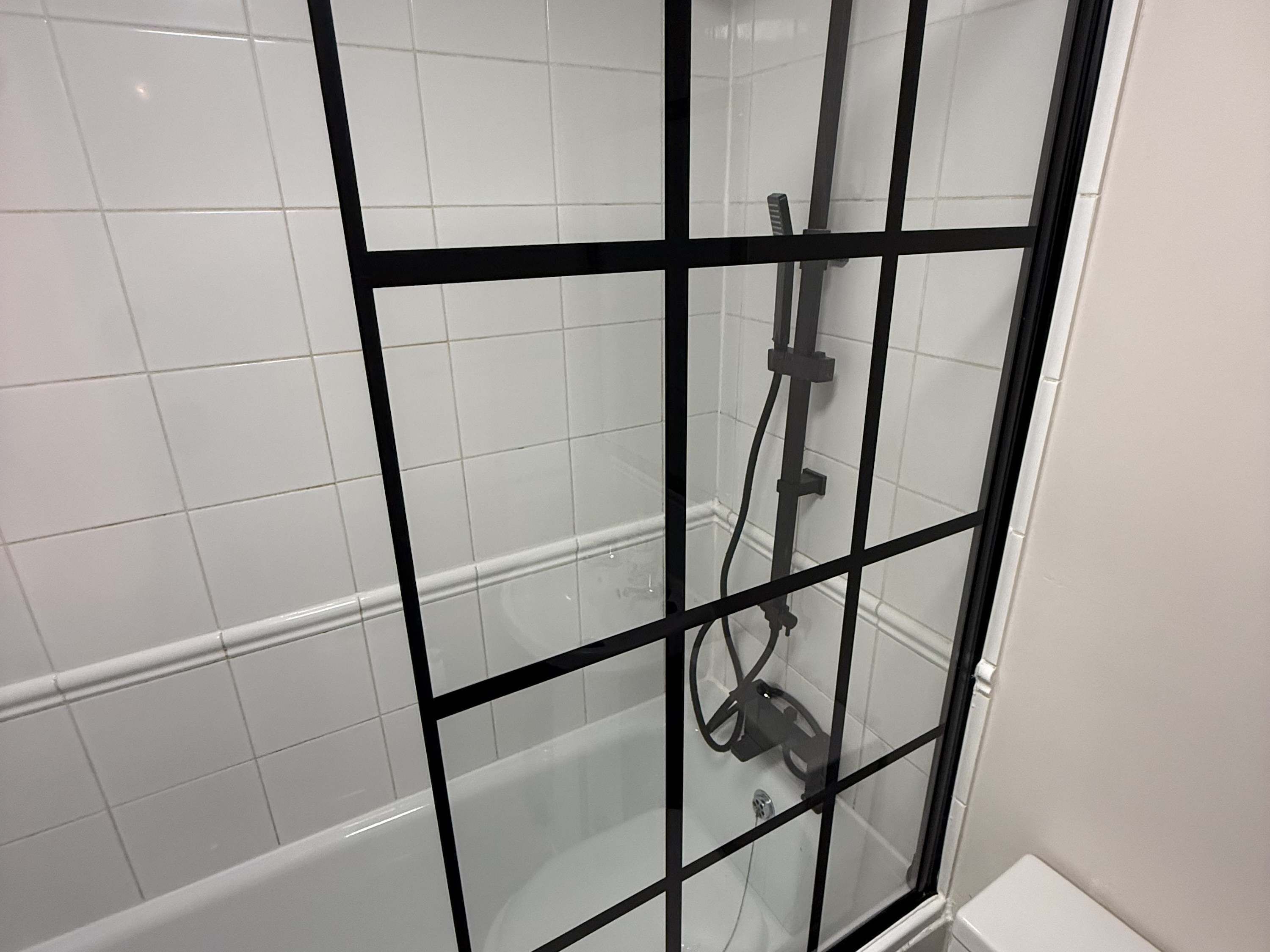 Une cabine de douche dotée d’une porte en verre et d’un cadre noir.